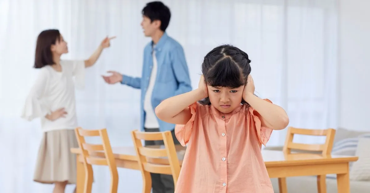 Criança tapando os ouvidos enquanto os pais discutem ao fundo, representando o impacto da alienação parental.