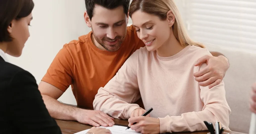 Casal feliz assinando documento de pacto antenupcial em cartório, simbolizando a escolha do regime de bens no casamento.