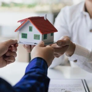 Mãos segurando uma miniatura de casa enquanto assinam documentos, simbolizando a partilha de bens em um processo de inventário.