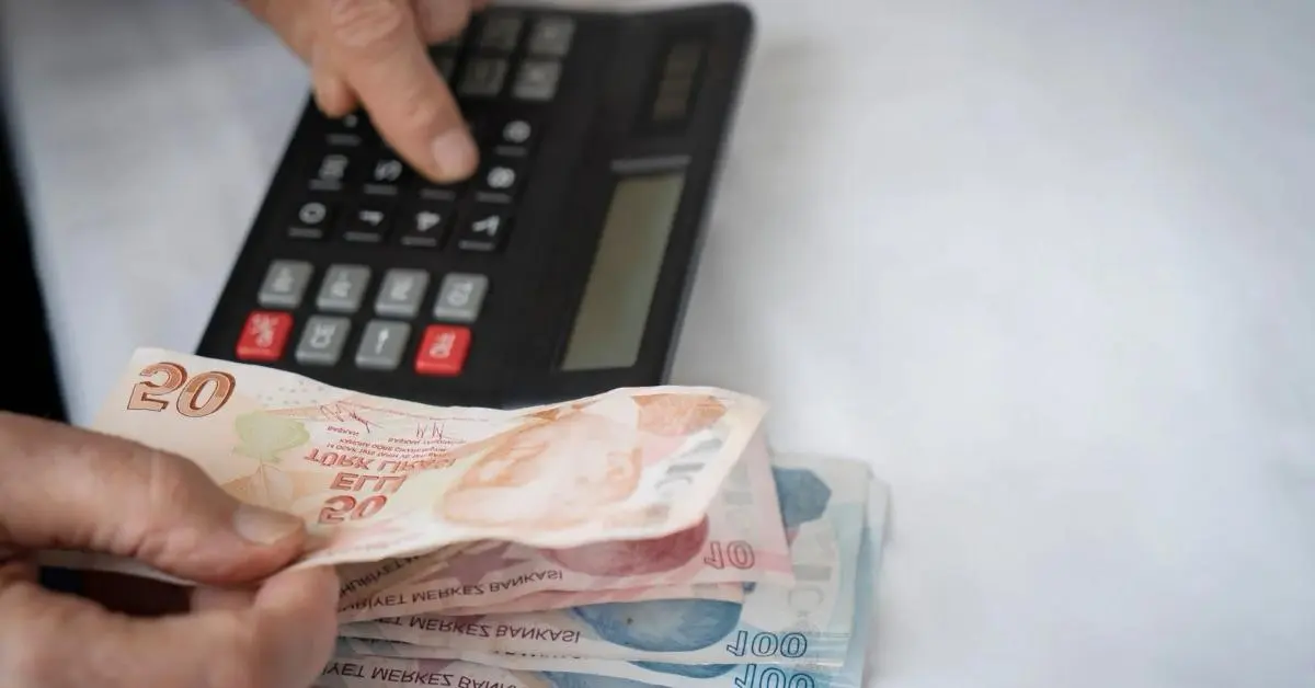 Pessoa utilizando calculadora e dinheiro estrangeiro, simbolizando pagamento de pensão alimentícia no exterior