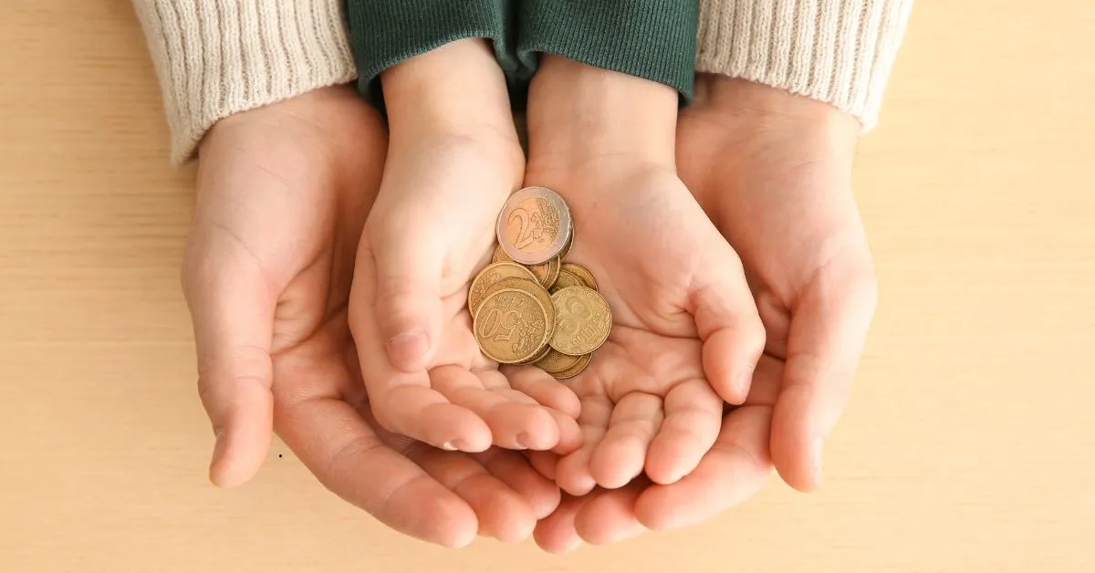 Mãos de adulto e criança segurando moedas, representando redução de pensão alimentícia
