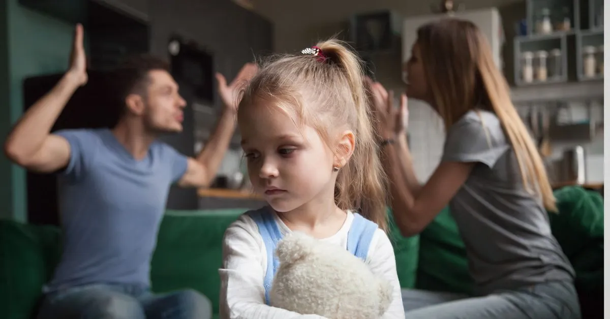 Criança triste segurando ursinho enquanto pais discutem, ilustrando os efeitos da alienação parental na saúde mental dos filhos