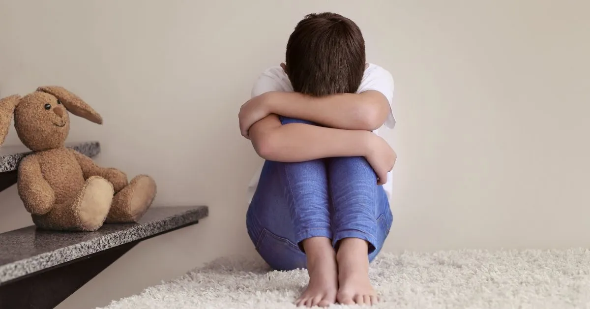 Criança sentada abraçando os joelhos, simbolizando o abandono afetivo e a falta de cuidado emocional prevista na Lei 15.240/2025.